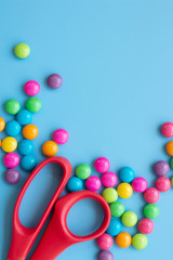 Sweet candies and red scissors on blue background with copy space. Homemade dessert concept