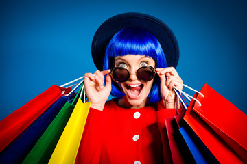 Portrait of surprised admired woman looking out glasses with wide open eyes mouth screaming holding colorful packets in hands enjoying seasonal sale having pleasure. Delight inspiration concept