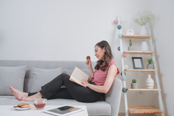 Happy young woman reading storybook on couch at home