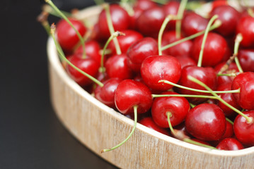 Fresh Cherries Fruit with leaves in Wooden Heart Shape Box, top view. Summer Red Berries. Black Background