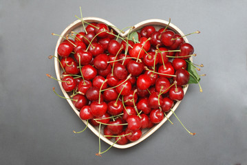 Fresh Cherries Fruit with leaves in Wooden Heart Shape Box, top view. Summer Red Berries. Black Background