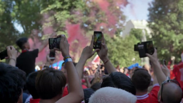 People with phone into hands records video on background crowd at festival in day time, football fans everywhere