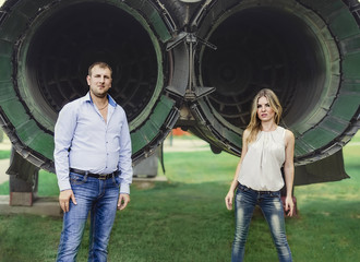 The young couple standing near the plane, looking at camera