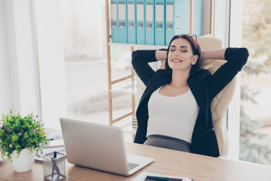 Portrait of glad charming woman holding hands behind head keeping eyes closed planing vacation weekend trip journey sitting at desk having supplies laptop on the table