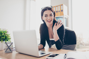 Portrait of sexy friendly woman bending over near desk gesturing palm hi sign having video call...