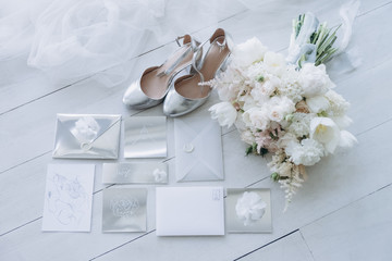 top view of stylish wedding invitations with bridal shoes and bouquet on wooden floor