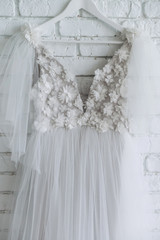 stylish wedding dress decorated with flowers hanging on white brick wall