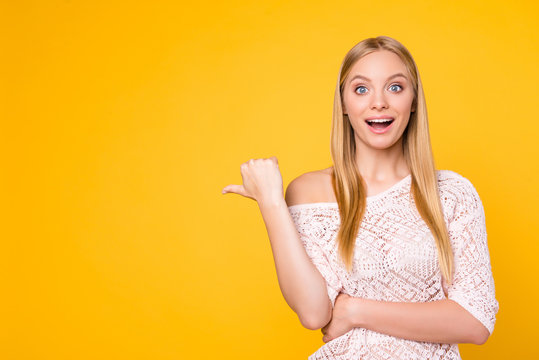 Portrait of wondered excited girl with wide open mouth eyes gesturing copy space empty place with thumb up looking at camera isolated on bright vivid yellow background