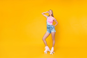 Fototapeta na wymiar Full size body portrait of pretty funky girl on roller skates gesturing v-sign near eye looking at camera isolated standing over yellow background