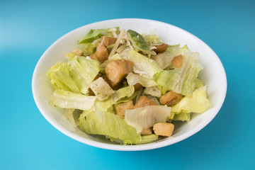 Appetizing salad of fresh vegetables, chicken pieces, toast in a white plate on a blue background close-up