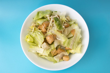 Appetizing salad of fresh vegetables, chicken pieces, toast and cheese in a white plate on a blue background close-up