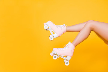 Cropped portrait of legs in pink vintage quad roller skates shoes isolated on yellow background, extreme balance concept, street outside urban lifestyle style, laser hair removal perfect skin