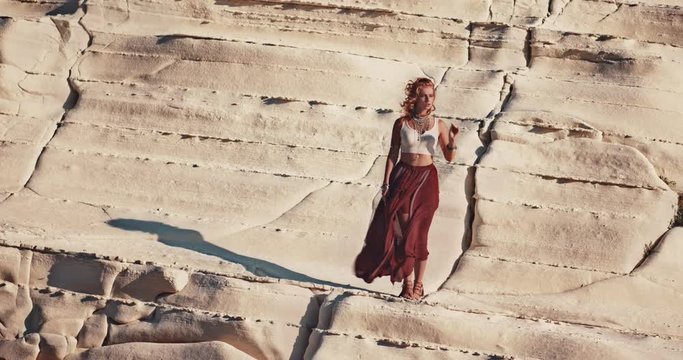 Young boho woman standing on white beach rock in summer