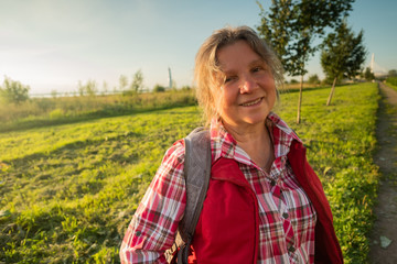 Close up portrait of happy older woman standing outside in summer on field background.