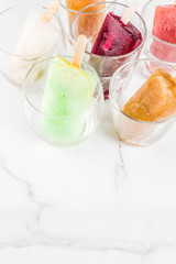 Summer party food ideas, frozen boozy alcohol cocktails popsicles - Prosecco, Vodka lime mojito, Champagne, Bellini, Margarita, Negroni etc white marble table copy space