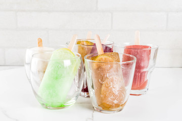 Summer party food ideas, frozen boozy alcohol cocktails popsicles - Prosecco, Vodka lime mojito, Champagne, Bellini, Margarita, Negroni etc white marble table copy space