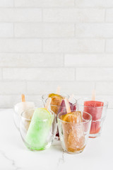 Summer party food ideas, frozen boozy alcohol cocktails popsicles - Prosecco, Vodka lime mojito, Champagne, Bellini, Margarita, Negroni etc white marble table copy space