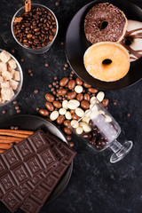 Top view of peanuts in chocolate, spilled on the dark board, next to chocolate tablets, donuts, brown sugar and coffee beans. Studio photo