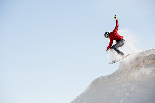 Photo of man in helmet with snowboard jumping from snowy mountain slope