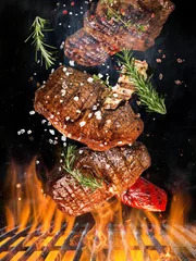Poster Tasty beef steak flying above cast iron grate with fire flames. © Lukas Gojda