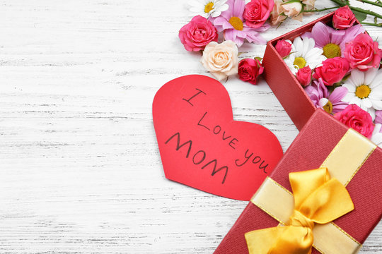 Gift, flowers and and card with words "I love you Mom" on wooden background. Greetings for Mother's Day