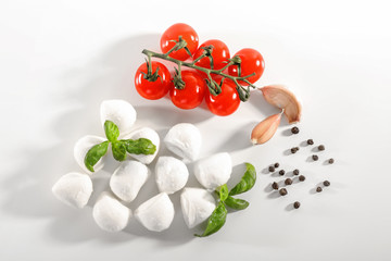 Mozzarella cheese balls, cherry tomatoes, garlic and basil on white background