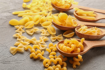 Different uncooked pasta and wooden spoons on grey table