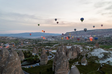 scenic view of pile of hot air balloons flying over cityscape and stone formations in Cappadocia, Turkey