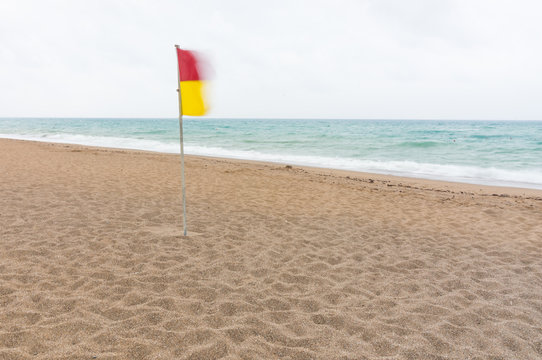 Red And Yellow Warning Flag On A Deserted Beach