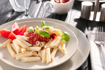 Plate of tasty penne pasta with bolognese sauce on table, closeup