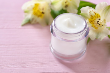 Fototapeta na wymiar Jar with cream and flowers on wooden background. Skin care cosmetics