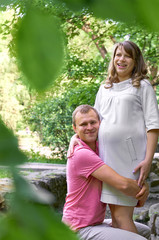 Fototapeta premium Handsome man is listening to his beautiful pregnant wife's tummy belly and smiling. Husband listening to his wife's belly. Happy pregnant family funny.