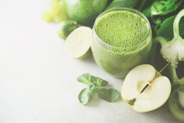 Glass with green health smoothie, kale leaves, lime, apple, kiwi, grapes, banana, avocado, lettuce. Sunlight bokeh. Copy space. Raw, vegan, vegetarian, alkaline food concept.