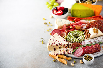 Traditional italian antipasto, cutting board with salami, cold smoked meat, prosciutto, ham, cheeses, olives, capers on grey background. Cheese and meat appetizer.