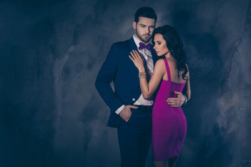 Portrait of brutal mr with bristle in tux with bow holding hand in pocket of pants embracing pretty charming mrs with booty bum isolated on grey background with copy space empty place