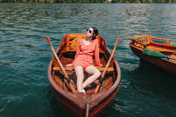 Obraz premium beautiful girl in sunglasses sitting on wooden boat on lake