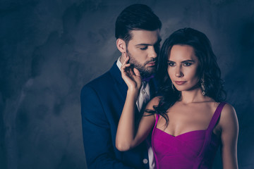 Portrait of pretty charming mrs in purple dress with jewelry half face mr in tuxedo bowtie holding hand in pocket of pants embracing his lover lovely attractive couple isolated on grey background - obrazy, fototapety, plakaty