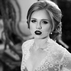 Obraz premium Blonde woman with elegant hairstyle wearing dress and white lace jacket, standing on garden terrace and leaning on balustrade decorated with large flower vases against shining sun on background.