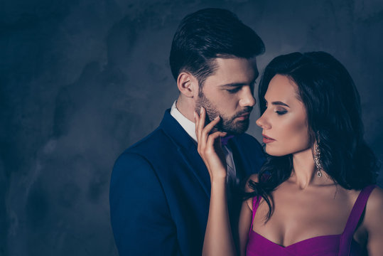 Portrait of pretty charming mrs in purple dress with jewelry half face mr in tuxedo bowtie holding hand in pocket of pants embracing his lover lovely attractive couple isolated on grey background