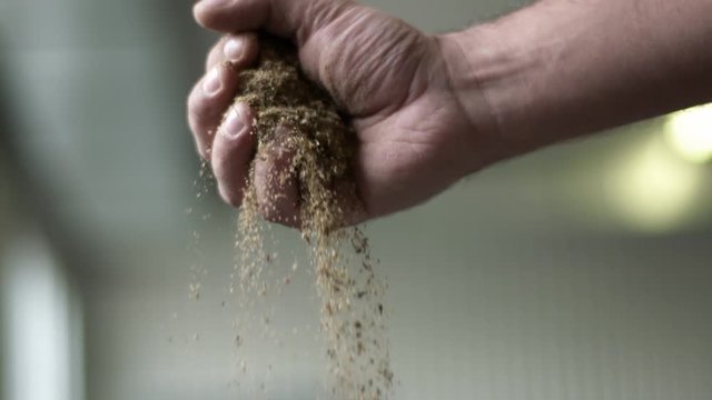 White hairy male's hand spread brown finely grin into linen bag through fingers in slow motion. Close up