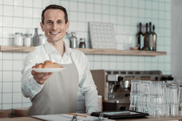 Fresh pastry. Delighted brunette expressing positivity while proposing tasty croissants