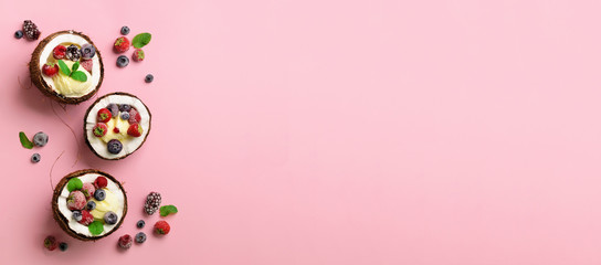 Coconut ice cream with fresh berries in coconuts halves on pink background with copy space. Top...