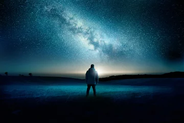 Fotobehang Een man staat met verwondering en verbazing te kijken terwijl de maan en het melkwegstelsel de nachtelijke hemel vullen. Nachtelijk landschap. Foto composiet. © James Thew