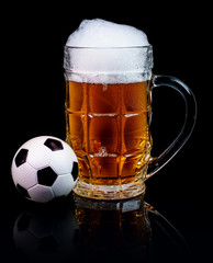 Glass of beer and a small soccer ball isolated on a black background.