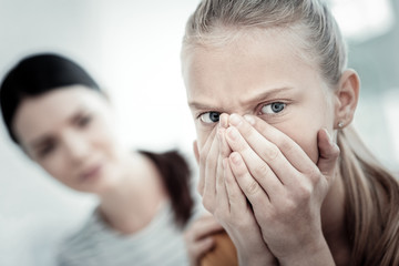 Unstoppable tears. Selective focus of pleasant crying teen girl covering her nose and staring aside with female psychologist posing on background