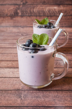 Blueberry yogurt in glass cups with fresh blueberries and mint on a wooden rustic table