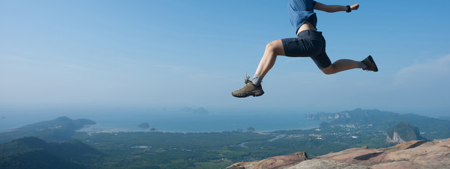 Young woman jumping on mountain peak cliff edge