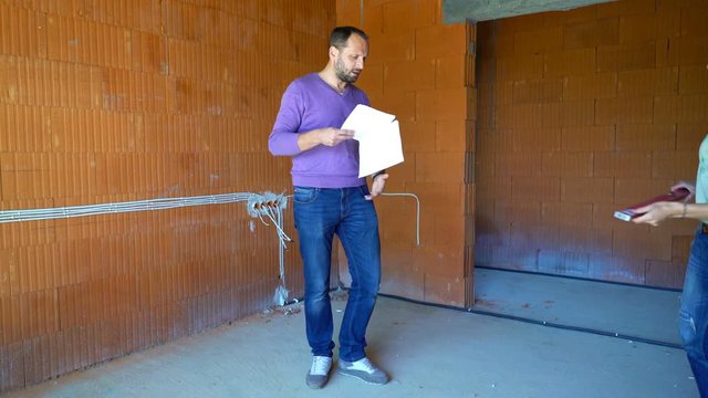 Couple with blueprints checking wall with level at their new house 
