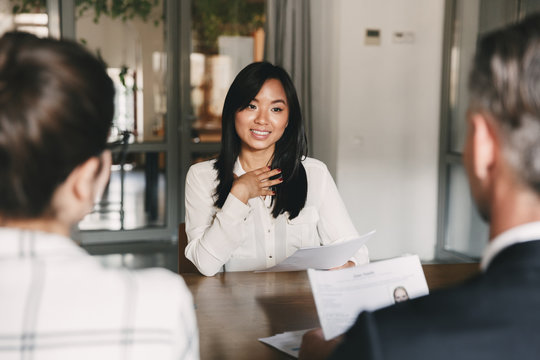 Business, career and placement concept - young asian woman smiling and holding resume, while sitting in front of mentor or managers during job interview