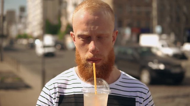 portrait giger man with beard standing on the street enjoy fresh drink in summer season. on the background heavy traffic in city